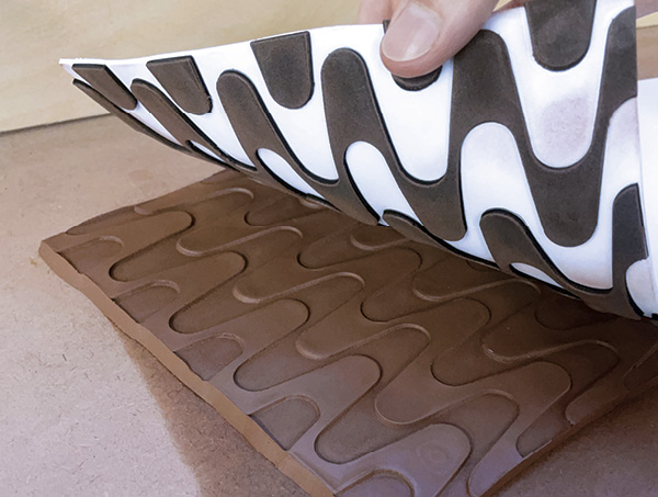 4 Cut around the template, removing excess clay. Gently peel the template away from the clay, revealing the textured slab.