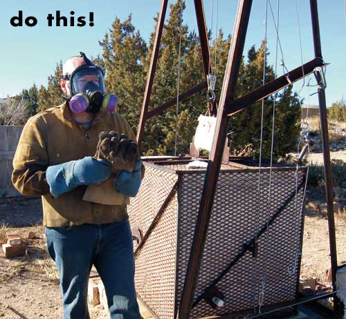 Standing next to the raku kiln, Lancaster demonstrates full respiratory protection. The blue mits are for removing large works from the kiln. In his hands, he is holding Kevlar gloves, which are used for turning the hot pieces over in the reduction barrels.