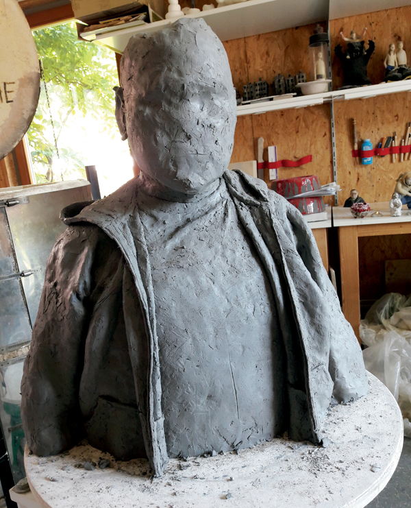 A Working directly on a kiln shelf, create a rough construction of the bust. Begin sketching the face onto the head. 