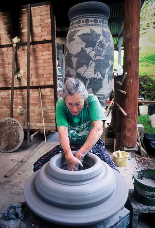 Sandy throwing a section for another of her big pots, like the one behind her positioned next to her car kiln. They were all thrown in separate large sections on the wheel then attached together before being painted with slip and carved using the sgraffito technique.