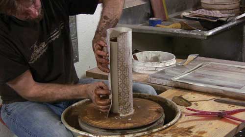 3 Carefully placing transfer newsprint around slip-coated cylinder.